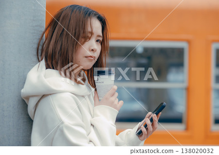 一位二十多歲的女性手捧咖啡站在火車站台上的肖像。 138020032