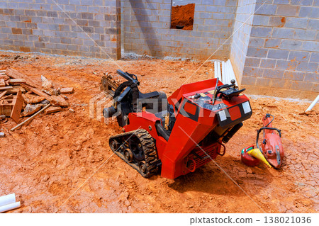 Small construction digging machine sits on dirt surface at building site with bricks pipes nearby Small construction digging machine sits on dirt surface at building site with bricks pipes nearby 138021036