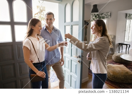 Realtor agent handing house keys to happy couple in doorway Realtor agent handing house keys to happy couple in doorway 138021134