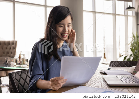 Happy young Asian professional woman analyzing paper sales report Happy young Asian professional woman analyzing paper sales report 138021142
