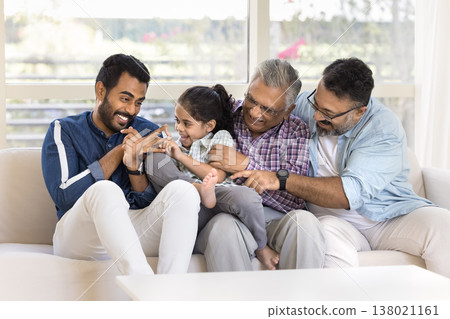 Multigenerational Indian male family playing together seated on couch Multigenerational Indian male family playing together seated on couch 138021161