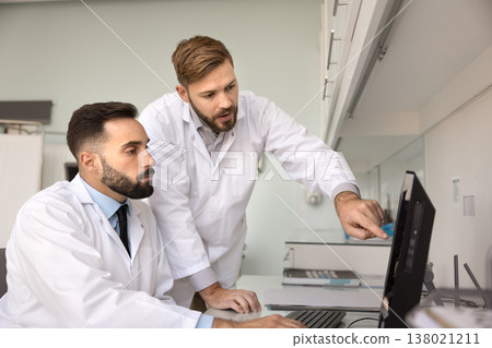 Professional team two male doctors analyzing files on pc screen Professional team two male doctors analyzing files on pc screen 138021211