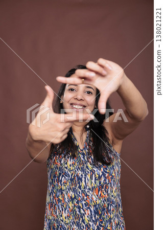 Smiling indian woman making photo frame gesture with fingers, looking at camera. Cheerful photographer posing portrait, front view studio medium shot, photography, imaginable photoshoot 138021221