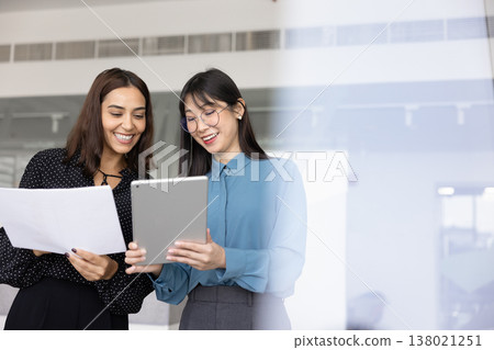 Cheerful young diverse businesswomen comparing electronic and paper reports Cheerful young diverse businesswomen comparing electronic and paper reports 138021251
