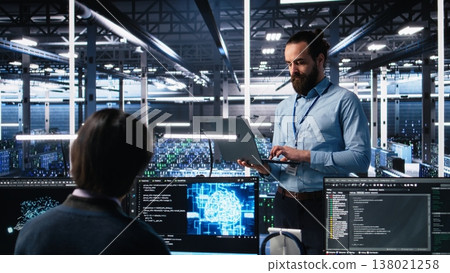Data center technician using laptop to monitor neural network AI LLM visualization. IT specialist in high tech facility using notebook to oversee servers powering machine learning processes, camera A 138021258