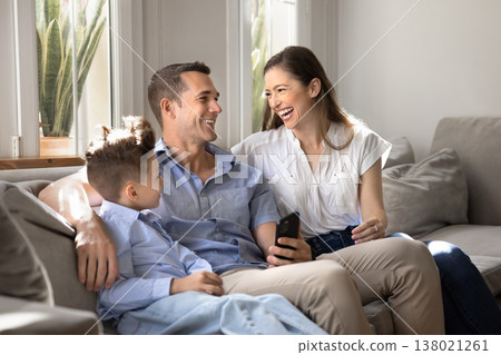Parents and child sitting on couch with smartphone Parents and child sitting on couch with smartphone 138021261