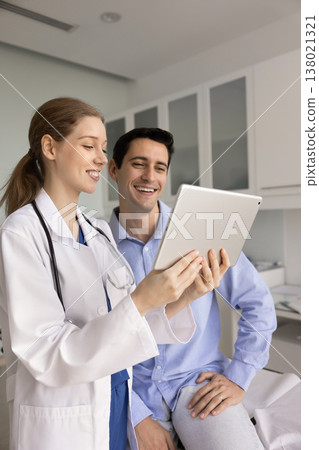 Doctor and patient looks at tablet screen with joyful expression 138021321