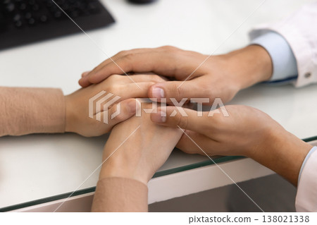 Doctor sits at table holding hands of female patient, closeup 138021338