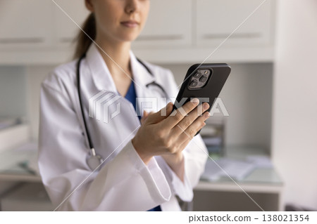 Close-up cropped view of female doctor in uniform using smartphone Close-up cropped view of female doctor in uniform using smartphone 138021354