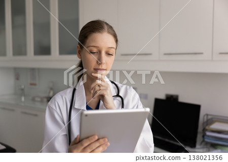 Young thoughtful woman nurse, healthcare specialist working on tablet Young thoughtful woman nurse, healthcare specialist working on tablet 138021356