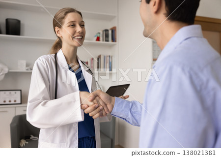 Happy Latina woman general practitioner shaking hands with man patient Happy Latina woman general practitioner shaking hands with man patient 138021381