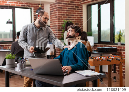 Millennial freelancer recovering after accident having neck pain wearing medical neck collar while working in brick wall startup office. Businessmen analyzing company turnover discussing business Millennial freelancer recovering after accident having neck pain wearing medical neck collar while working in brick wall startup office. Businessmen analyzing company turnover discussing business 138021409