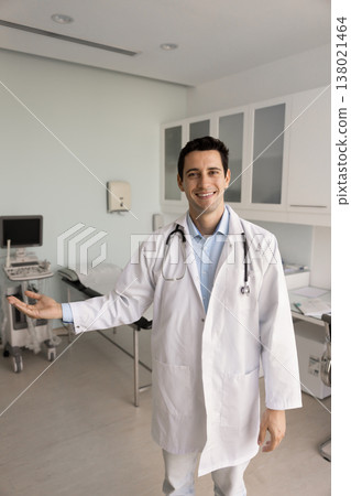 Cheerful male doctor smiles and gestures with hand, welcoming patient 138021464