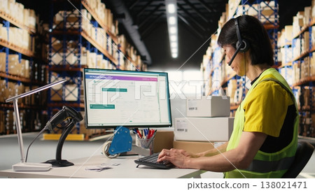 Call center employee assisting customers in a fulfillment center, handling inventory control and package tracking. Asian man resolving issues related to delivery delays or wrong addresses. Camera A. Call center employee assisting customers in a fulfillment center, handling inventory control and package tracking. Asian man resolving issues related to delivery delays or wrong addresses. Camera A. 138021471