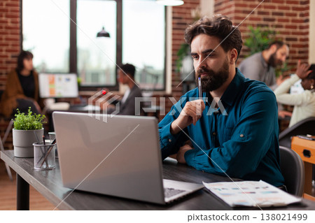 Doubtful pensive entrepreneur having uncertain think about marketing project analyzing company turnover on computer. Businessman working at business collaboration in startup office. Diverse team 138021499