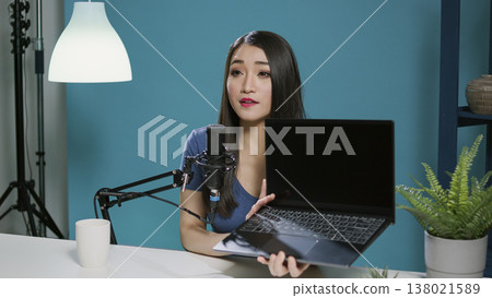 Asian woman reviewing laptop computer on social media podcast, recording live network video. Female vlogger broadcasting product recommendation with modern gadget and online technology. 138021589