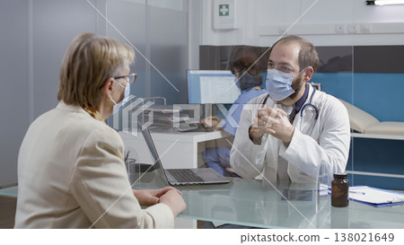 Retired woman attending checkup consultation with medic, wearing face mask in medical cabinet. Elder person asking for healthcare advice from physician at examination appointment. Retired woman attending checkup consultation with medic, wearing face mask in medical cabinet. Elder person asking for healthcare advice from physician at examination appointment. 138021649