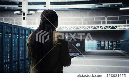 Engineer in server hub using laptop to upgrade rigs for increase in workload capacity using AI deep learning. Data center employee uses artificial intelligence to improve processing speed, camera A 138021655