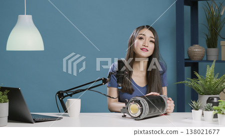 Female blogger recommending studio light accessory on camera, filming online product review with modern lighting equipment. Smiling influencer using broadcast gadget for channel. Tripod shot. 138021677