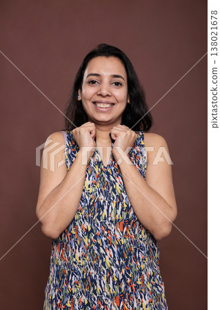 Smiling cute indian woman holding clenched fists on cheeks portrait. Cheerful lady touching face with hands, model standing with carefree expression, looking at camera, front view 138021678