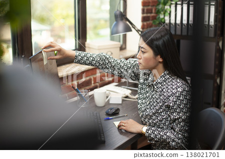 Professional woman adding post it reminders to computer screen, analyzing business analytics and preparing for upcoming deadlines at office desk. Female employee tracks her tasks with adhesive note. Professional woman adding post it reminders to computer screen, analyzing business analytics and preparing for upcoming deadlines at office desk. Female employee tracks her tasks with adhesive note. 138021701