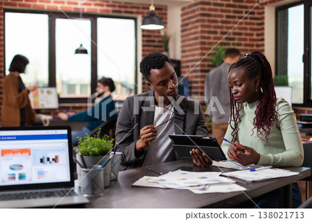 Entrepreneur man holding tablet computer showing company statistics to colleague discussing marketing strategy during business meeting in startup office. Multiethnic team working at financial project Entrepreneur man holding tablet computer showing company statistics to colleague discussing marketing strategy during business meeting in startup office. Multiethnic team working at financial project 138021713