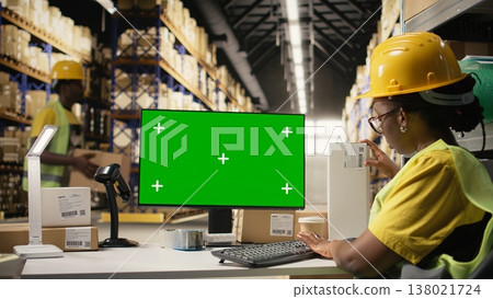 Woman warehouse clerk handling shipment protocols with copy space on pc, working on large business operations for retail industry. Depot filled with cardboard boxes on racks. Camera A. Woman warehouse clerk handling shipment protocols with copy space on pc, working on large business operations for retail industry. Depot filled with cardboard boxes on racks. Camera A. 138021724