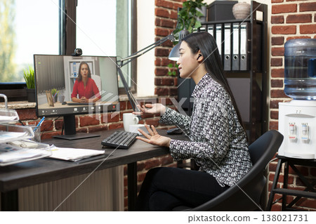 Financial advisor seated at table, speaks to businesswoman on a video call, discussing marketing strategies and plans. Asian female manager having an online conversation with her remote coworker. Financial advisor seated at table, speaks to businesswoman on a video call, discussing marketing strategies and plans. Asian female manager having an online conversation with her remote coworker. 138021731