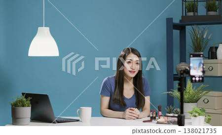 Female blogger recording makeup tutorial on camera in studio, talking about beauty products and glam cosmetics on social media vlog. Lifestyle influencer giving beauty tips on channel. 138021735
