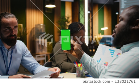 Diverse company workers hold phone with isolated chroma key, meeting with employees in a late night briefing. People focusing on company development and making a pitch for a project. Camera A. Diverse company workers hold phone with isolated chroma key, meeting with employees in a late night briefing. People focusing on company development and making a pitch for a project. Camera A. 138021761