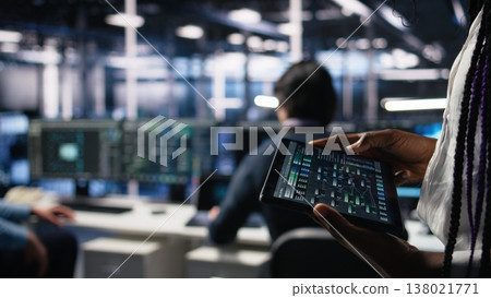 Close up of data center engineer using tablet to review code for automation scripts. Server farm system administrator using device, monitoring error logs for debugging processes, camera A 138021771