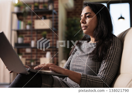 Business woman sitting on couch and working, doing remote office job on laptop pc at home. Using computer to work on data report, sending email and browsing internet for research plan. 138021790