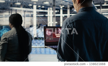 Engineer in server room receives critical error popup on laptop screen, dealing with urgent system issues. Data center worker gets notification about hardware problems affecting performance, camera B 138021888