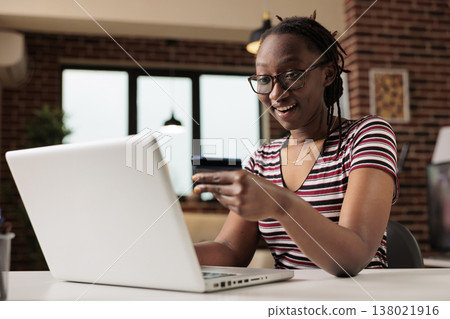 Happy consumer holding credit card, buying products in internet store, online retail shopping concept. Smiling person making purchase using laptop, buyer paying for order at home, mid shot Happy consumer holding credit card, buying products in internet store, online retail shopping concept. Smiling person making purchase using laptop, buyer paying for order at home, mid shot 138021916