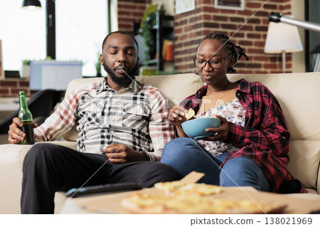 Relaxed people eating chips from bowl and drinking beer, having fun together with fast food takeaway meal. Enioying takeout delivery and watching movie or film on television, entertainment. 138021969