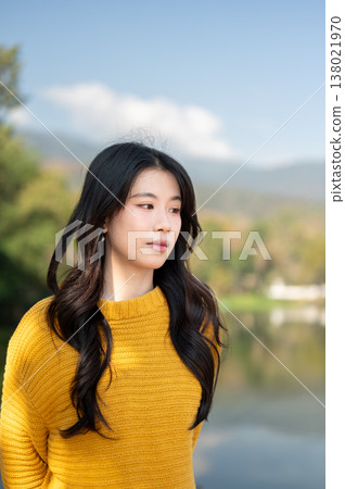 Pretty asian woman in yellow sweater standing with water nature scenery in background under blue sky Pretty asian woman in yellow sweater standing with water nature scenery in background under blue sky 138021970