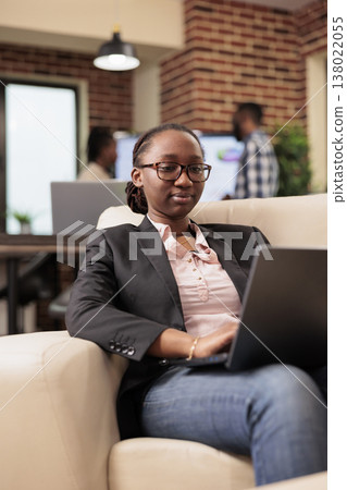 African american project manager analyzing data on laptop, using online research information to create business report. Browsing internet website to work on company management, startup office. 138022055