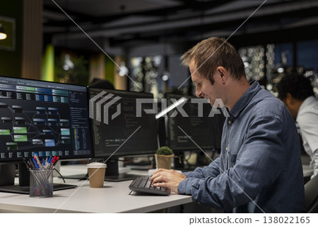 Happy engineer at office desk reviewing AI system metrics, monitoring performance dashboards. Cheerful tech company employee tuning neural networks using program on computer 138022165