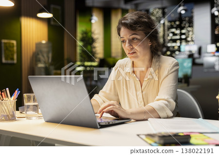 Employee works after hours organizing and scheduling tasks for a corporate project. Surrounded by files, she focuses on budgeting and objectives to achieve company targets at night. Employee works after hours organizing and scheduling tasks for a corporate project. Surrounded by files, she focuses on budgeting and objectives to achieve company targets at night. 138022191