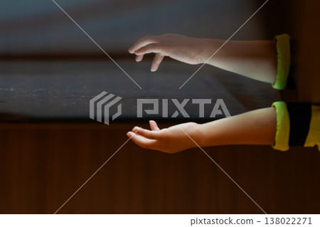 Child hand touching an illuminated interactive surface with reflection representing human connection with technology and digital interaction. Child hand touching an illuminated interactive surface with reflection representing human connection with technology and digital interaction. 138022271