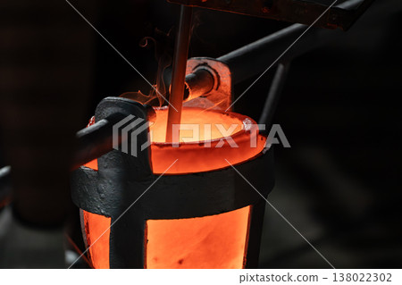 Close up of molten metal being poured into a heated crucible during casting showing intense heat, flame, and thermal energy. 138022302