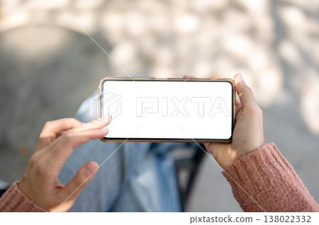 A woman's hand holding and touching white screen phone sitting on outdoor bench over concrete floor. A woman's hand holding and touching white screen phone sitting on outdoor bench over concrete floor. 138022332