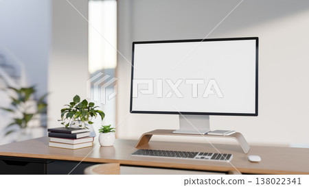 White screen computer with books and potted plants on wooden table across wall in modern style room. White screen computer with books and potted plants on wooden table across wall in modern style room. 138022341
