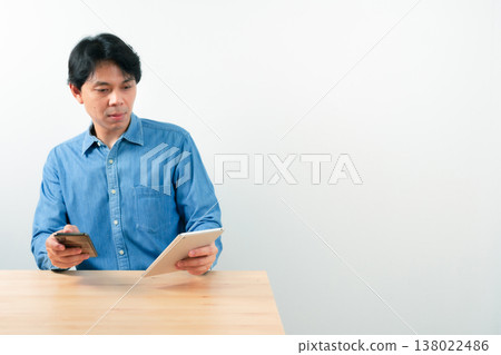 asian business man 30s to 40s with blue shirt use tablet for check profit of his startup business with good feeling and white isolated background asian business man 30s to 40s with blue shirt use tablet for check profit of his startup business with good feeling and white isolated background 138022486