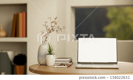 White screen laptop with book and plants on round wooden table across window an shelf in living room White screen laptop with book and plants on round wooden table across window an shelf in living room 138022631
