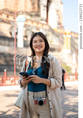 Pretty asian woman holding phone standing and looking around the ancient pagoda of buddhist temple. 138022715
