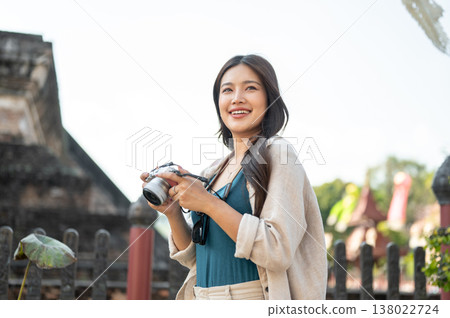 Pretty asian woman standing holding camera and looking around the ancient pagoda of buddhist temple. 138022724
