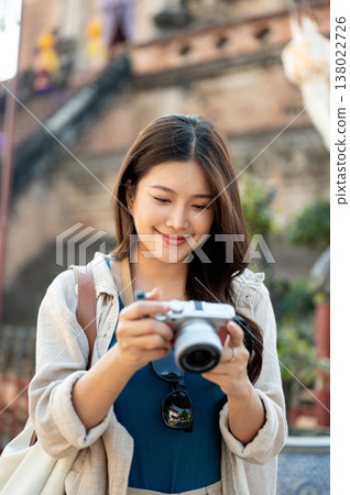Pretty asian woman holding looking through camera standing aside ancient pagoda in buddhist temple. 138022726