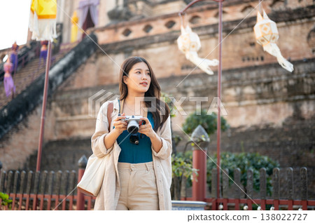 Pretty asian woman holding camera looking around as standing aside ancient pagoda in buddhist temple 138022727