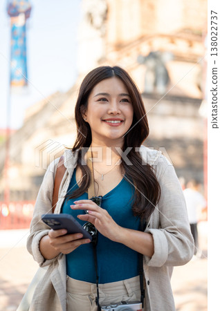 Pretty asian woman holding phone standing and looking around the ancient pagoda in buddhist temple. 138022737